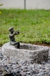 Bronzeskulptur "Flötenspieler Finn" als Wasserspeier auf einem Stein im Garten