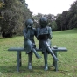 Bronzeskulptur Sitzende Mädchen mit grüner Patina auf einer Bank im Garten 