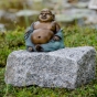 Bronzeskulptur "Happy Buddha" von der Seite auf einem Stein