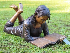 Bronzeskulptur Paula liegend mit Ihrem Buch im Garten
