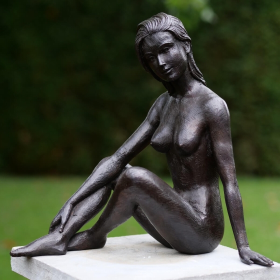 Bronzeskulptur Sitzende Frau mit brauner Patina im Garten 