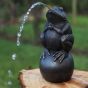 Bronzeskulptur Frosch auf Kugel als Wasserspeier auf Baumstamm im Garten 