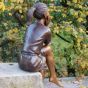 Bronzeskulptur Sitzendes Mädchen beim nachdenken von hinten im Garten 